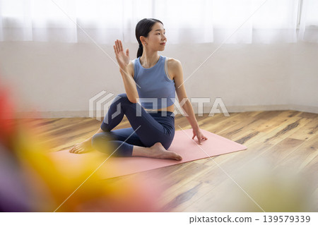 一位中年日本女性在明亮的窗邊，於瑜珈墊上練習雙魚座瑜珈姿勢。 139579339