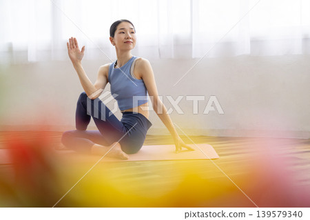 一位中年日本女性在明亮的窗邊，於瑜珈墊上練習雙魚座瑜珈姿勢。 139579340