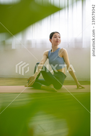 A middle-aged Japanese woman performs the Pisces pose in yoga on a mat by a bright window. A middle-aged Japanese woman performs the Pisces pose in yoga on a mat by a bright window. 139579342
