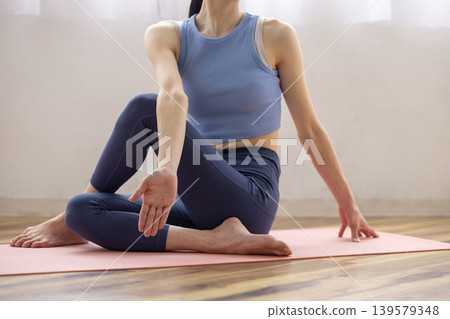 A middle-aged Japanese woman performs the Pisces pose in yoga on a mat by a bright window. 139579348