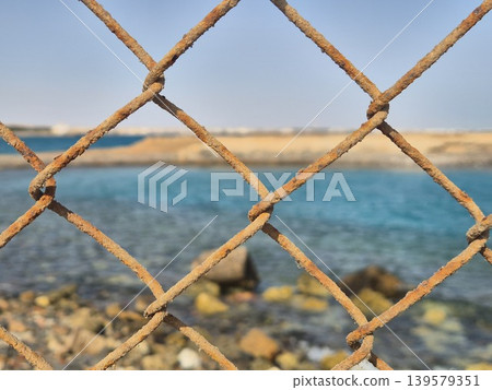 Rusty chain link fence by blurred seascape 139579351