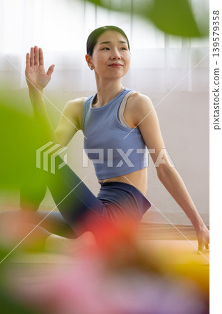 一位中年日本女性在明亮的窗邊，於瑜珈墊上練習雙魚座瑜珈姿勢。 139579358