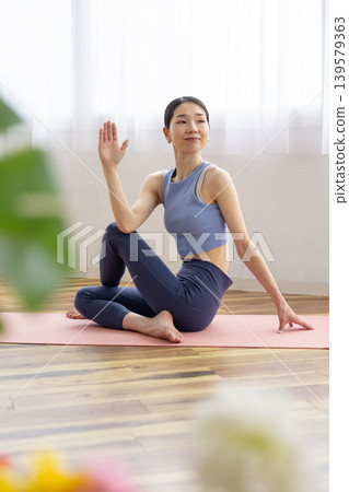 一位中年日本女性在明亮的窗邊，於瑜珈墊上練習雙魚座瑜珈姿勢。 139579363