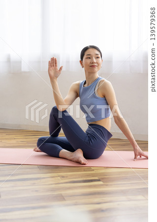 A middle-aged Japanese woman performs the Pisces pose in yoga on a mat by a bright window. A middle-aged Japanese woman performs the Pisces pose in yoga on a mat by a bright window. 139579368