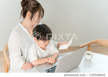 一位單親媽媽一邊抱著孩子，一邊看著電腦和銀行存摺。 139580042