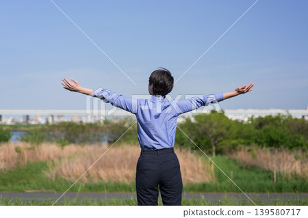 A woman's back view as she relaxes with her arms outstretched under a blue sky. A woman's back view as she relaxes with her arms outstretched under a blue sky. 139580717