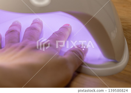 A woman is curing her gel nails with a UV light. A woman is curing her gel nails with a UV light. 139580824
