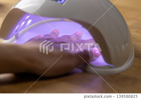 A woman is curing her gel nails with a UV light. A woman is curing her gel nails with a UV light. 139580825