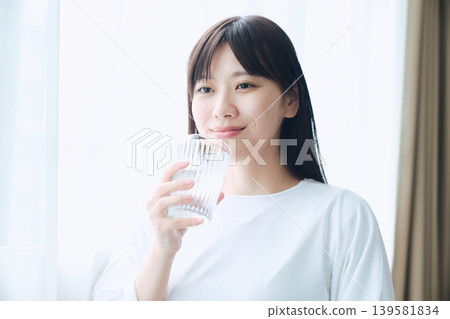 A woman drinking water by the window in the morning. 139581834