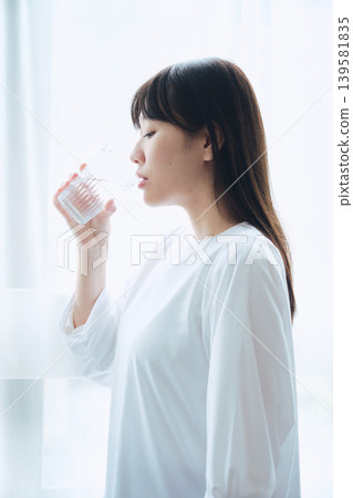 清晨,一位女士在窗邊喝水。 清晨,一位女士在窗邊喝水。 139581835