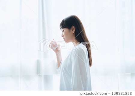 清晨，一位女士在窗邊喝水。 139581838
