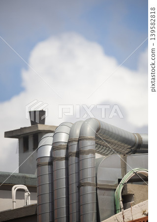 Pipes connect to roof of building under blue sky with white clouds in background during daytime Pipes connect to roof of building under blue sky with white clouds in background during daytime 139582818