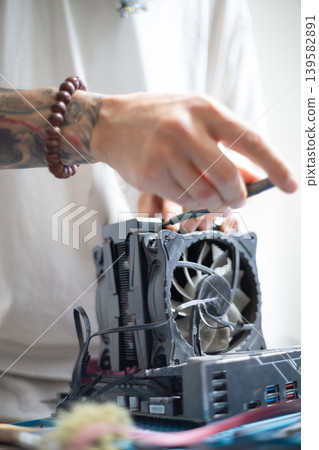 Person repairs computer hardware with a CPU fan in a workspace during daylight hours Person repairs computer hardware with a CPU fan in a workspace during daylight hours 139582891