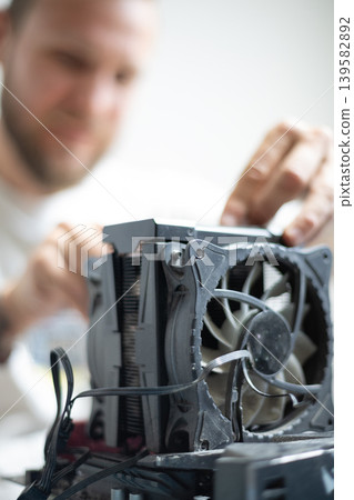 Man works on computer hardware with cooling unit in a workshop during daytime Man works on computer hardware with cooling unit in a workshop during daytime 139582892