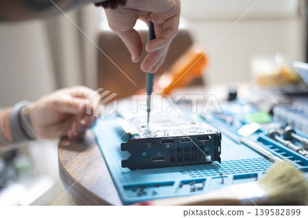 Person working on a computer part on a table with tools and materials in a room during daylight hours Person working on a computer part on a table with tools and materials in a room during daylight hours 139582899