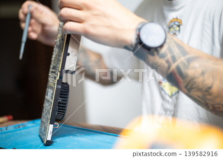 Man works on a computer graphic card repair at home with tools in early morning light 139582916