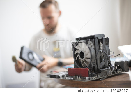 Man working on computer hardware in a home workspace during daytime 139582917