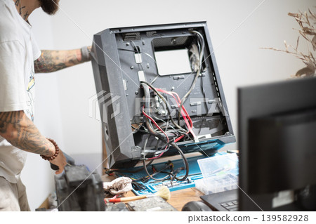 Man working on a computer case at a desk in a modern workspace during daytime Man working on a computer case at a desk in a modern workspace during daytime 139582928
