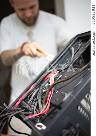 Person repairs computer case with wires and tools while focused on task in a well-lit room Person repairs computer case with wires and tools while focused on task in a well-lit room 139582931