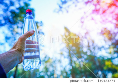 Water bottle in athlete's hand during a hike in woods. Water is used for hydration Water bottle in athlete's hand during a hike in woods. Water is used for hydration 139583274