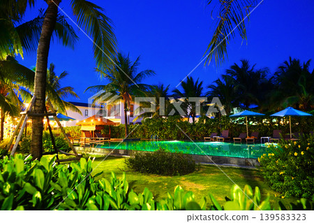 Night view of tropical resort pool with palm trees and lounge chairs in night. Tropical resort Night view of tropical resort pool with palm trees and lounge chairs in night. Tropical resort 139583323