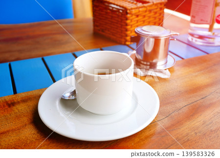 Cup of coffee on table in cafe in bright daytime. White cup witn coffee rests on plate with spoon Cup of coffee on table in cafe in bright daytime. White cup witn coffee rests on plate with spoon 139583326