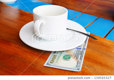 Coffee cup on cafe table with hundred dollars bill. Payment coffee drink on breakfast Coffee cup on cafe table with hundred dollars bill. Payment coffee drink on breakfast 139583327