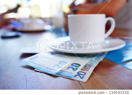 Coffee cup on table with Euro money bill in cafe. Payment coffee drink on breakfast. EC Bill money Coffee cup on table with Euro money bill in cafe. Payment coffee drink on breakfast. EC Bill money 139583338