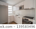 Modern kitchen with white cabinets, stainless steel appliances, and a clean countertop. Natural light enters through the window, creating a bright atmosphere. 139583496