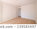 Empty room with light wooden flooring and white walls. A door leads to another space. The room is bright and spacious, ideal for interior design or renovation concepts. 139583497