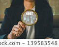 Businesswoman holding magnifying glass with cost reduction concept, highlighting financial strategy in office. 139583548