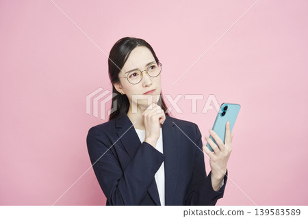 A businesswoman struggling with her smartphone (pink background) A businesswoman struggling with her smartphone (pink background) 139583589