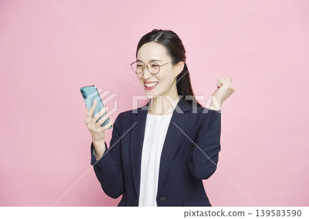 A businesswoman looks at her smartphone and makes a triumphant gesture. A businesswoman looks at her smartphone and makes a triumphant gesture. 139583590