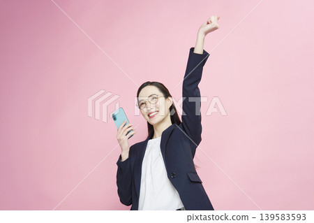A businesswoman looks at her smartphone and makes a triumphant gesture. A businesswoman looks at her smartphone and makes a triumphant gesture. 139583593