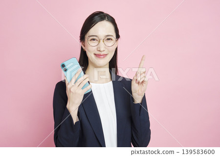 A businesswoman holding her smartphone and pointing. A businesswoman holding her smartphone and pointing. 139583600