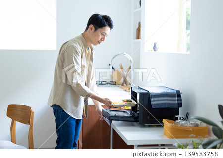 一名男子正在用微波爐加熱冷凍便當盒。 一名男子正在用微波爐加熱冷凍便當盒。 139583758