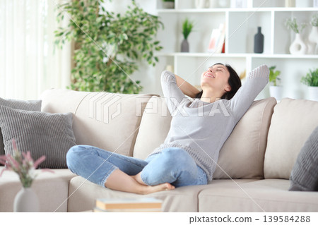Happy asian woman relaxing on a sofa in a house Happy asian woman relaxing on a sofa in a house 139584288