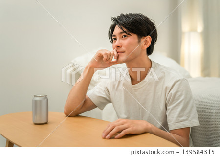 A young Asian man drinking canned beer and canned chu-hi (a type of Japanese alcoholic beverage) at night in his bedroom at home. 139584315