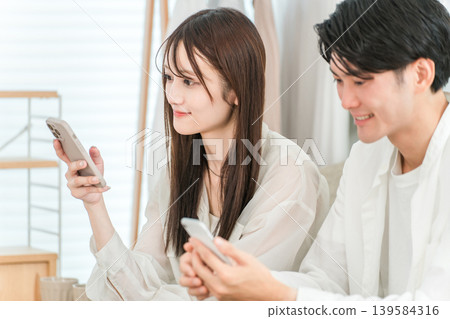 A young Asian couple sitting on the sofa in the living room at home and talking while looking at their smartphones 139584316