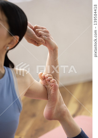 一位中年日本女性在明亮的窗邊，於瑜珈墊上練習鴿子式。 139584418
