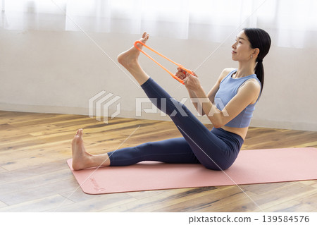 A middle-aged Japanese woman in yoga wear exercising with a resistance band. 139584576