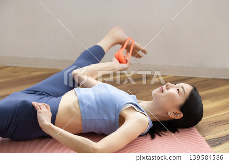 A middle-aged Japanese woman in yoga wear exercising with a resistance band. A middle-aged Japanese woman in yoga wear exercising with a resistance band. 139584586