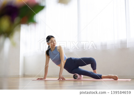 A middle-aged Japanese woman in yoga wear uses a foam roller for self-massage. A middle-aged Japanese woman in yoga wear uses a foam roller for self-massage. 139584659