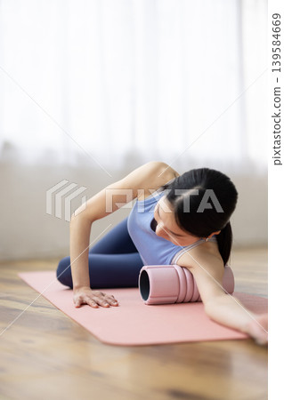 一位身穿瑜珈服的中年日本女性正在使用泡沫軸進行自我按摩。 139584669