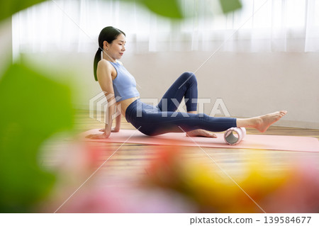 A middle-aged Japanese woman in yoga wear uses a foam roller for self-massage. A middle-aged Japanese woman in yoga wear uses a foam roller for self-massage. 139584677
