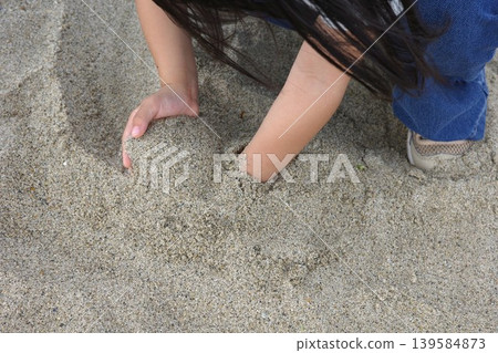 Close-up of a child's hands playing in the sand on the beach. Close-up of a child's hands playing in the sand on the beach. 139584873