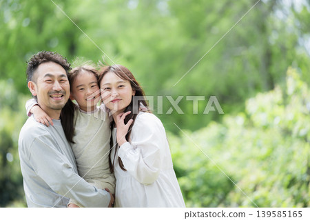 一張特寫照片,一家三口面帶微笑,依偎在綠意盎然的植物叢中,展現出幸福和親密的家庭畫面,他們都直視著鏡頭。 一張特寫照片,一家三口面帶微笑,依偎在綠意盎然的植物叢中,展現出幸福和親密的家庭畫面,他們都直視著鏡頭。 139585165