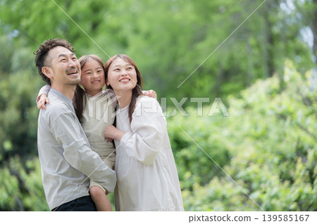 A close-up shot of a family of three smiling and huddled together amidst the fresh greenery, an image of happiness and family bonds, looking towards the future. A close-up shot of a family of three smiling and huddled together amidst the fresh greenery, an image of happiness and family bonds, looking towards the future. 139585167