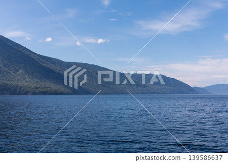 Wide view of Lake Teletskoye shoreline and Altai Mountains under blue sky Wide view of Lake Teletskoye shoreline and Altai Mountains under blue sky 139586637