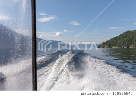 Speedboat wake on Teletskoye Lake with mountain shoreline and blue sky Speedboat wake on Teletskoye Lake with mountain shoreline and blue sky 139586643